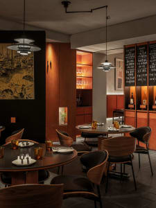 Well-lit, modern-look restaurant interior with wooden tables, black leather chairs, and industrial-style lighting.