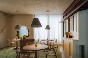 Modern restaurant interior with wooden tables, fabric curtains, and a window showcasing the outdoors.