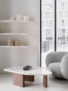 A minimalist living area featuring a white marble coffee table and gray upholstered sofa in front of a large window.