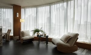 A minimalist living room with a modern, cozy aesthetic, featuring fabric and wood materials, and large windows with sheer cur