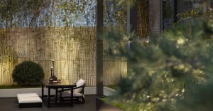 A minimalist outdoor dining area featuring bamboo plants, a stone table, and glass candle holders.
