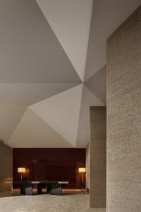 A modern office lobby featuring geometric ceiling designs, concrete walls, and sleek table setup.