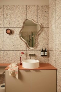A modern bathroom featuring a unique patterned wall with a circular mirror, white sink, and peach-colored countertop.
