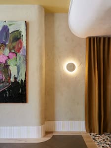 A modern residential interior with a textured wall, a circular wall lamp, and a gold curtain.