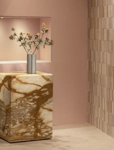 A modern marble table featuring a vase of flowers in a silver vase against a pink wall and beige tiled floor.