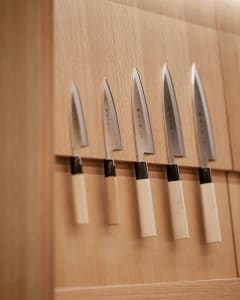 Set of five wooden-handle kitchen knives displayed on a wooden wall background.