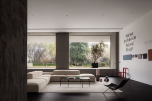 Minimalist living room with concrete walls and furniture, large windows overlooking greenery, and a modern coffee table.