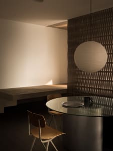 Modern minimalist dining room with glass table and pendant light fixture.