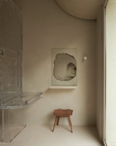 A minimalist interior featuring an acrylic desk and abstract artwork on a muted beige wall.