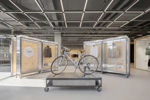 A modern minimalist exhibit showcasing bicycle and clothing products in a clean, industrial-style room with glass and metal d
