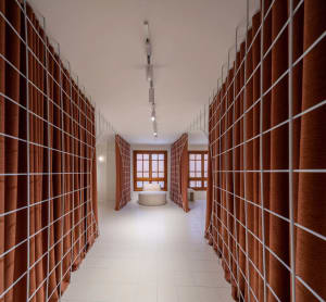 A modern corridor with textile walls and white flooring, featuring seating areas and grid-like structures.