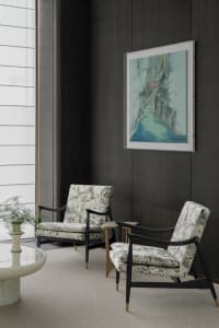 A modern living room featuring two armchairs with textured fabric upholstery, a round coffee table, and a framed abstract pai
