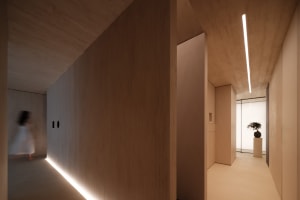 A minimalist interior featuring a corridor with concrete walls and floor, illuminated by a linear light fixture.