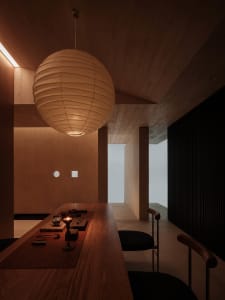 A minimalist tea room with wooden walls and floor, featuring a wooden counter and seating area, illuminated by a spherical pe
