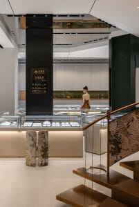 Interior of a modern jewelry store with glass display cases, wooden stair railings, and a metal pillar.
