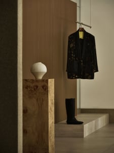 A minimalist clothing store with a wooden interior featuring a vase, coat, and boots.