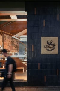 Modern restaurant exterior featuring black tiles and concrete materials, with a branded sign and staircase interior in the ba