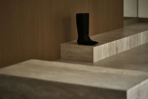 Modern minimalist shoe display made of concrete, featuring sleek black boots on a raised platform.