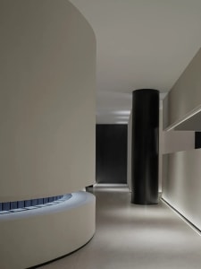 Modern minimalist corridor with curved walls and black cylindrical columns.