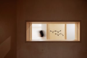 A rectangular window inset into a wooden wall, with a mural of interconnected letters inside.