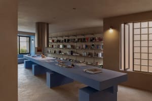 A spacious, industrial-style library with a concrete floor and walls, featuring a long table with books and a bookshelf fille