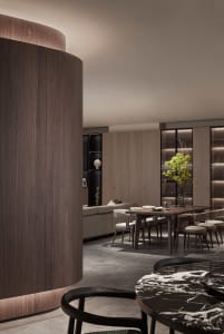 Modern dining room with wooden walls and chairs, marble table, and greenery centerpiece.