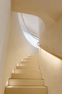 A modern staircase with concrete steps and walls, illuminated with small lights on the risers.