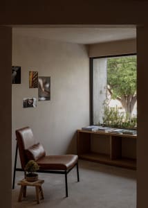 A modern living room with concrete walls and wooden accents, featuring a cozy corner seat and a window with greenery outside.