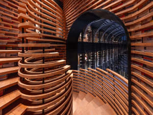 Modern bookstore interior with spiral wooden shelves and a glass-walled reading area.