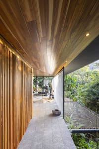 Indoor gym with wooden slats and concrete floor, featuring modern fitness equipment and lush greenery outside.