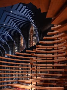 A modern library interior featuring wavy shelves and warm wooden lighting.