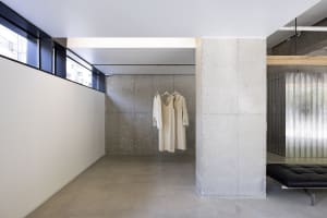 Creme-colored minimalist clothing items displayed on a concrete wall within a minimalist interior space.