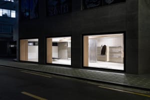 A modern retail storefront with illuminated interiors and concrete materials.