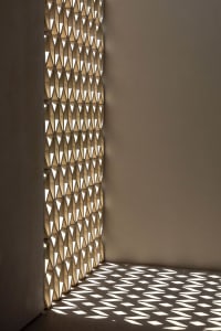 An architectural interior featuring illuminated wooden panels casting geometric shadows on the floor.