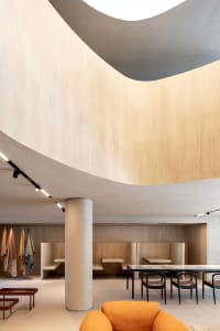 A minimalist restaurant interior with wooden seating, concrete walls, and metal accents.
