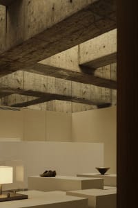 A minimalist interior space featuring concrete walls and ceiling beams, with simple furniture and decorative objects.