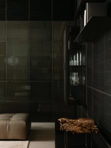 A modern residential interior with taupe leather seating, wood and glass furniture, and dark wooden walls.