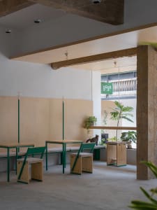 Modern cafe interior with concrete and wooden elements, including tables, chairs, and plants.