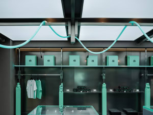 A modern storefront with green lighting and mixed materials, featuring shelves with boxes and clothing items.