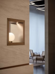 A minimalist lighting frame with a frosted glass sphere on a textured wall.
