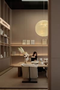 A modern office with a woven fiber rug on the floor and a bookshelf containing various books and a vase with orchids.