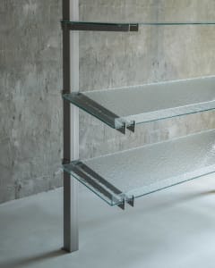 A minimalist glass shelf rack mounted on a concrete wall, featuring transparent glass shelves.
