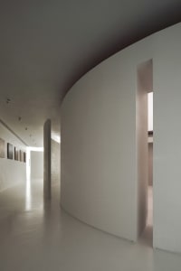 A minimalist interior space featuring a concrete corridor with white walls and a curved wall.