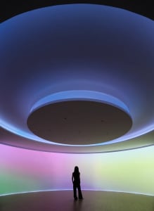 A person standing in a room with a circular light installation featuring LED lighting in shades of purple, blue, and green.