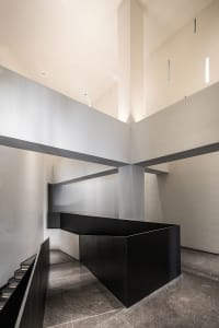 A contemporary interior space featuring a black cube structure and concrete walls and floor.