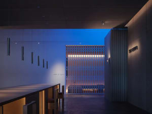 A minimalist bar featuring wooden stools, metal ceiling lights, and a wooden wall with a grid design.