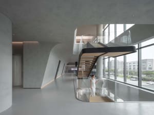 Industrial-style corporate lobby featuring concrete walls, glass walls, and a staircase with stainless steel railings.