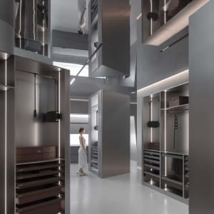 Photograph of a modern, minimalist wardrobe interior with glass, metallic, and wooden materials, featuring sleek, open shelve