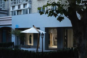 A modern retail storefront featuring a white parasol, wooden structure, and glass display windows.