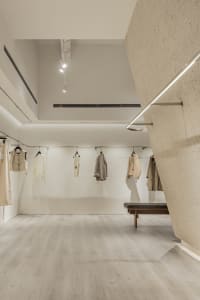 Modern retail store interior with minimalist design, neutral-toned materials, and clothing on display.